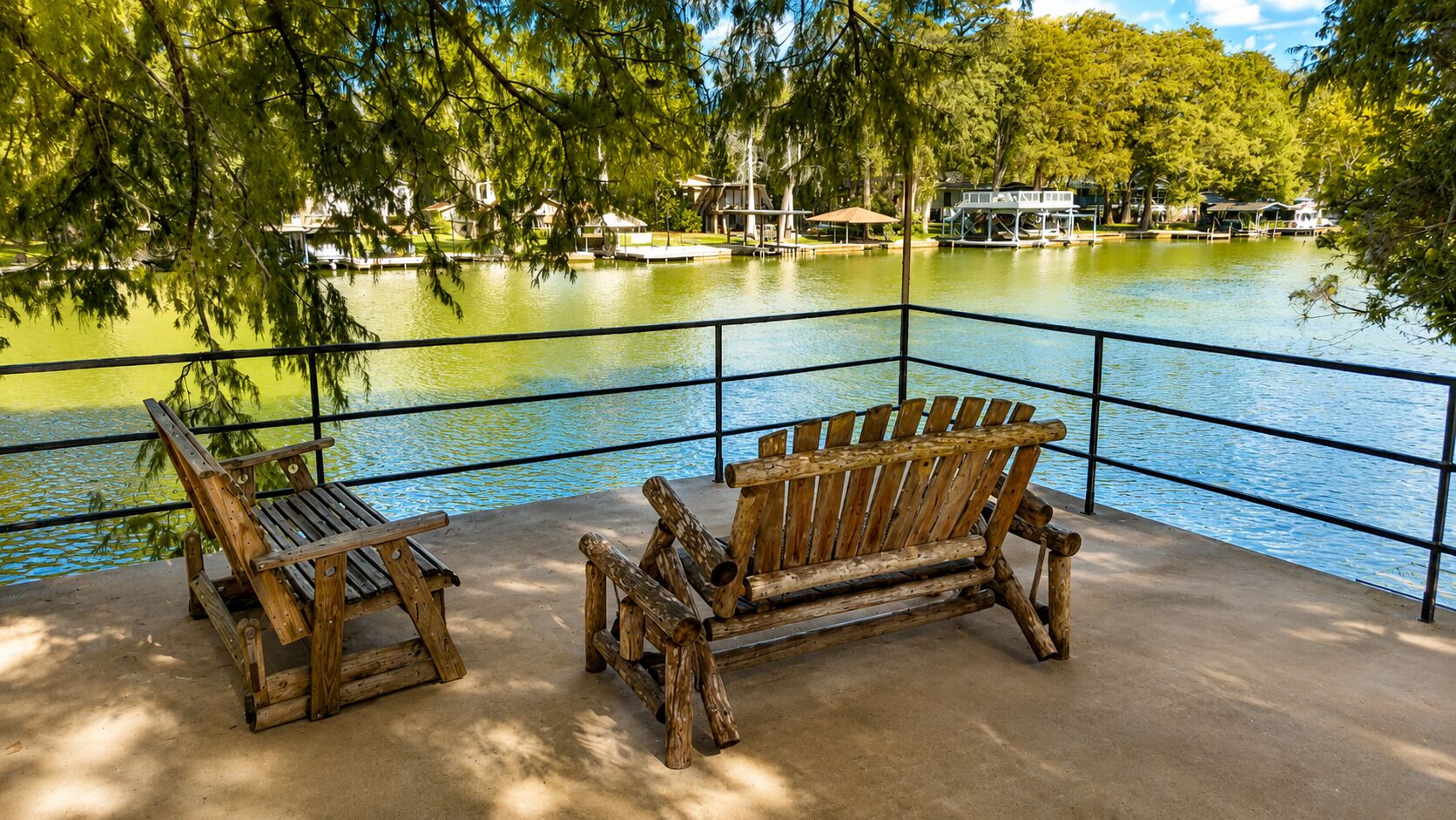 Um banco e uma cadeira de madeira perto de um lago, com corrimão de metal.