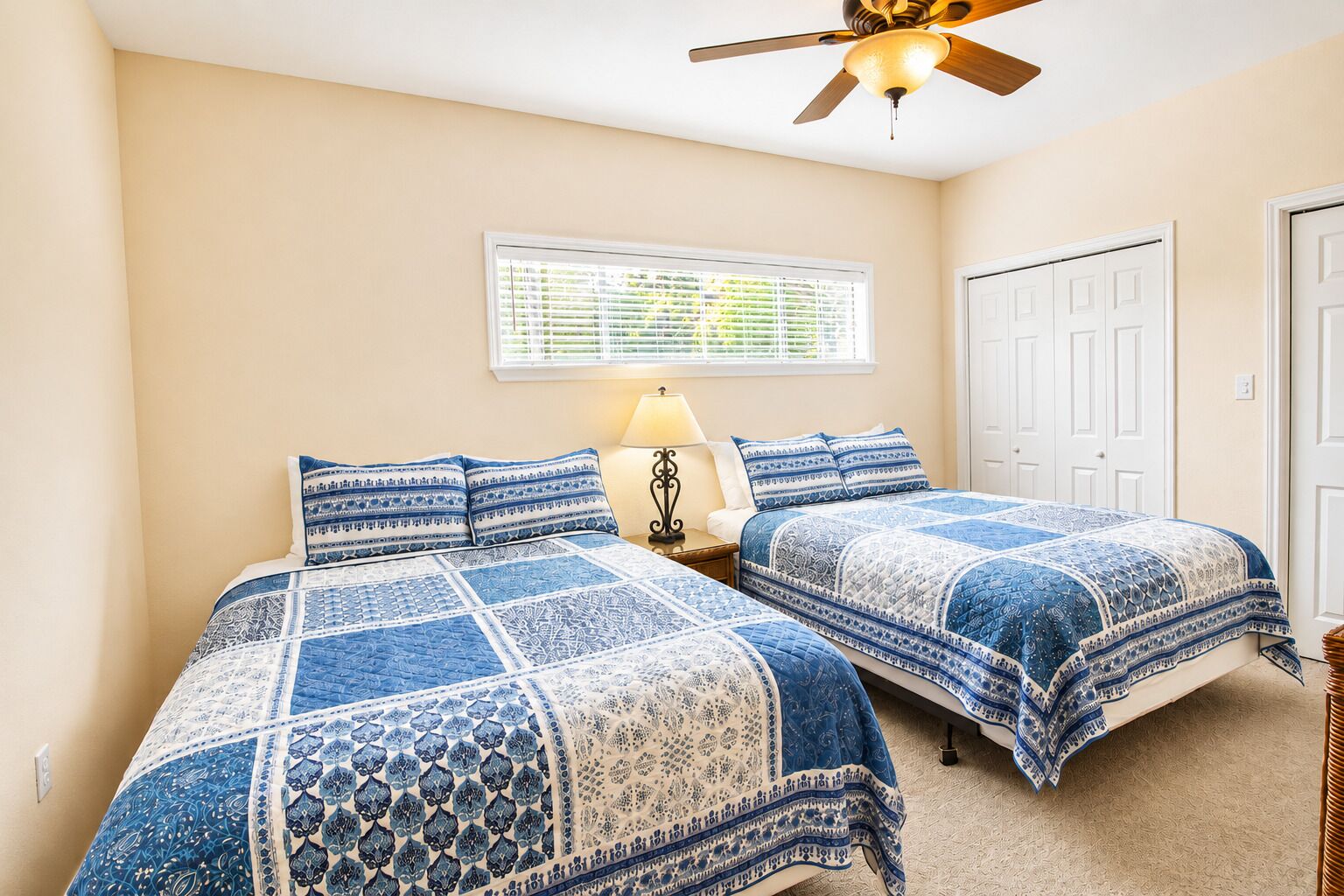 A bedroom with two beds, a ceiling fan, a window with blinds, and a door.
