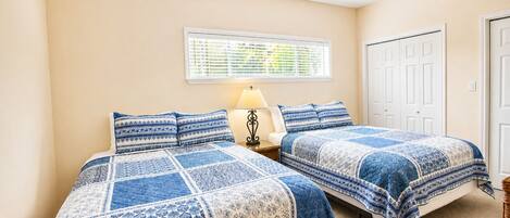 A bedroom with two beds, a ceiling fan, a window with blinds, and a door.