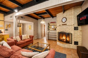 Una sala de estar acogedora con chimenea, un conjunto de sofás y un televisor montado en la pared.