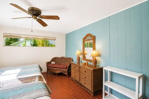 Un dormitorio con cama, una silla, cómoda, espejo y ventilador de techo.