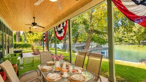 An outdoor dining area with a table set for four, surrounded by chairs, and overlooking a body of water with trees and a bridge in the background. - Funshine | Riverfront house in Mc Queeney with guest house, river views, grill (McQueeney)