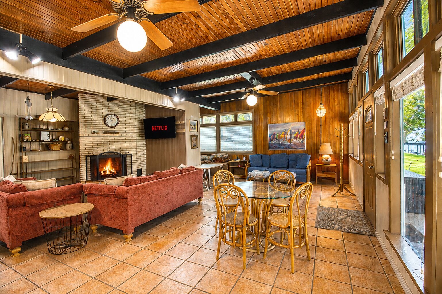 A cozy living room with a fireplace, a sofa, a dining table with chairs, and a television mounted on the wall.