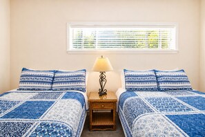 Un dormitorio con dos camas, una mesita de noche, una lámpara y una ventana con persianas.