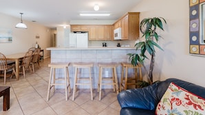 A kitchen with wooden cabinets, a white refrigerator, a microwave, and a coffee maker. There are three wooden stools and a dining table with chairs. A large potted plant is in the corner. - 3BR | 5 min Drive to Schlitterbahn | Pool, Hot Tub (New Braunfels)
