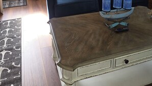 Een woonkamer met een houten vloer, twee donkerblauwe banken, een salontafel met drie blauwe kaarsen, een televisie aan de muur en een schilderij.