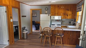 Een gezellig compacte leefruimte met een kitchenette, houten kastjes, een eethoek met stoelen en een bank.