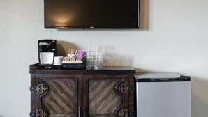 En minibar med en kaffebryggare, glas och snacks, en platt-TV ovanför och ett litet kylskåp nedanför.