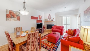 Ein Wohnzimmer mit Kamin, roten Sofas, einem Esstisch mit gemusterten Stühlen und einem Fernseher.