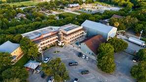 An aerial view of a building complex with multiple parking lots, a large central building, and surrounding greenery. - 3BR Riverfront Condo | Balcony | Pool | W/D | Snowbirds Welcome (New Braunfels)