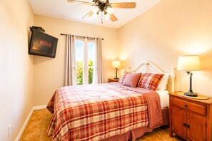 A bedroom with a bed, a television mounted on the wall, a ceiling fan, and a window with curtains. - 3BR Riverfront Condo | Balcony | Pool | W/D | Snowbirds Welcome (New Braunfels)