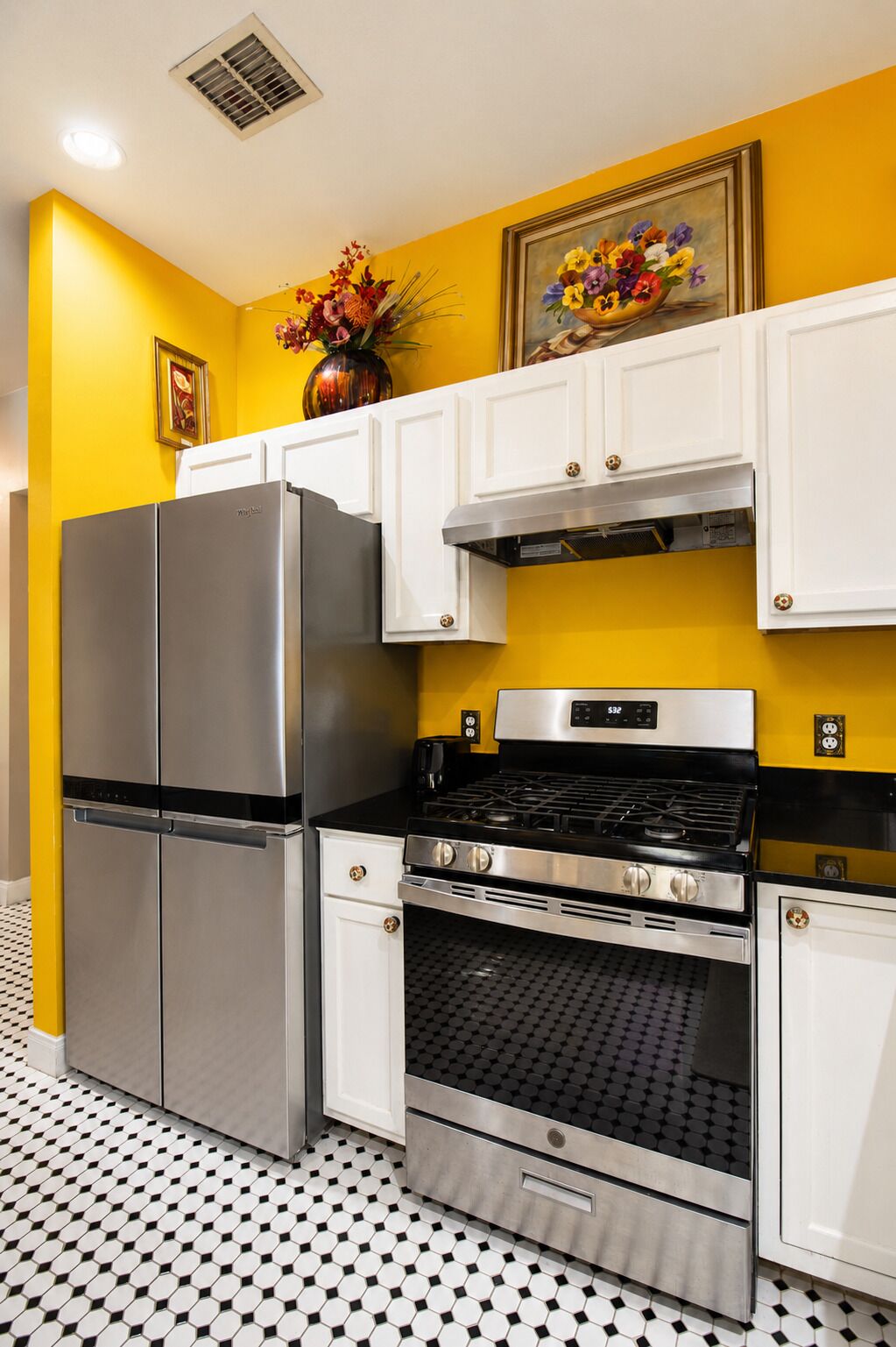 A kitchen with a stainless steel refrigerator, oven, and stove, white cabinets, and a yellow wall.