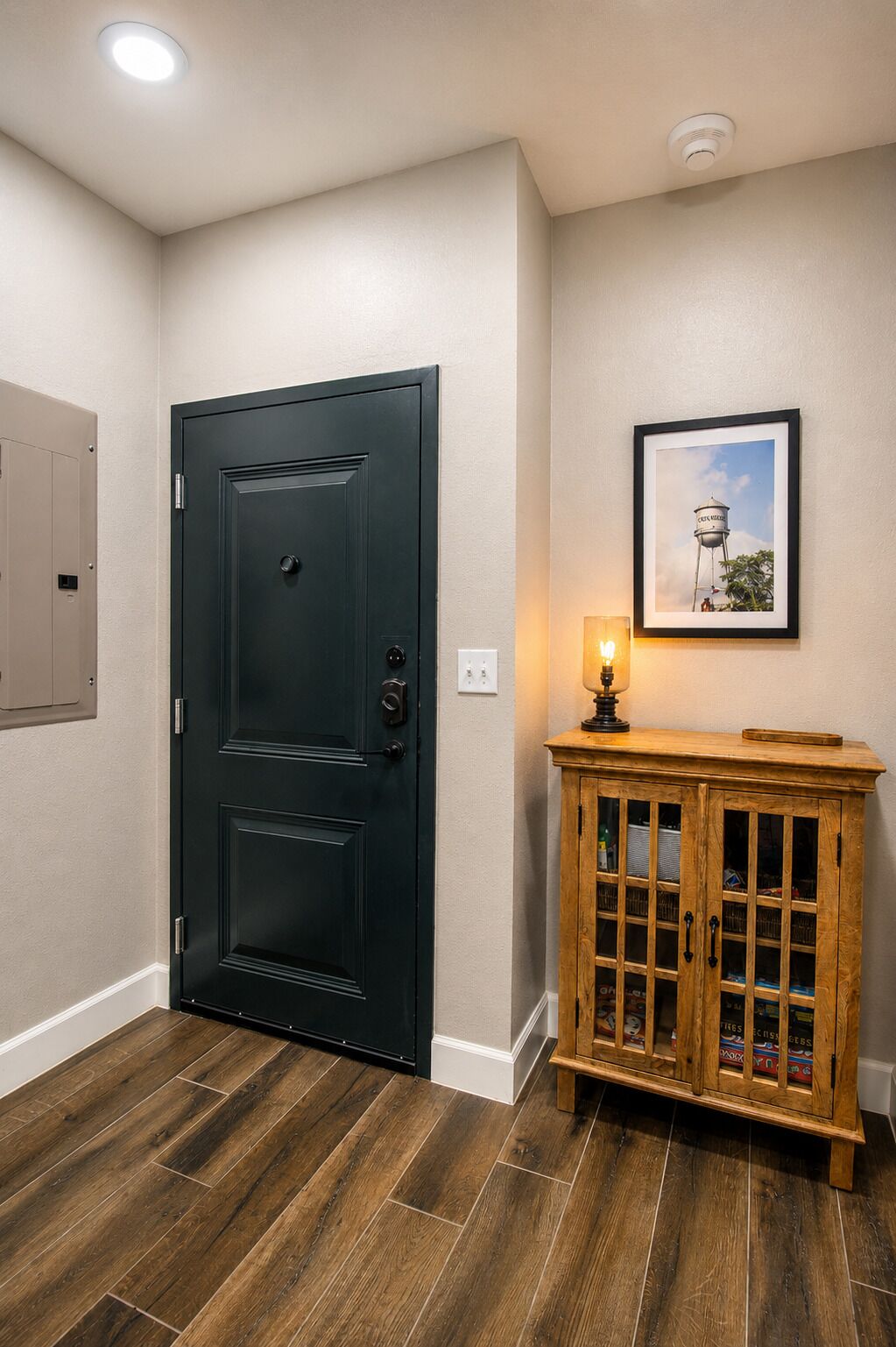 Une pièce avec une porte noire, un meuble en bois doté de portes en verre, un tableau encadré accroché au mur et un luminaire fixé sur le meuble.