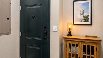Una habitación con una puerta negra, un mueble de madera con puertas de cristal, un cuadro en la pared y una lámpara sobre el mueble.