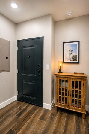 Une pièce avec une porte noire, un meuble en bois doté de portes en verre, un tableau encadré accroché au mur et un luminaire fixé sur le meuble.
