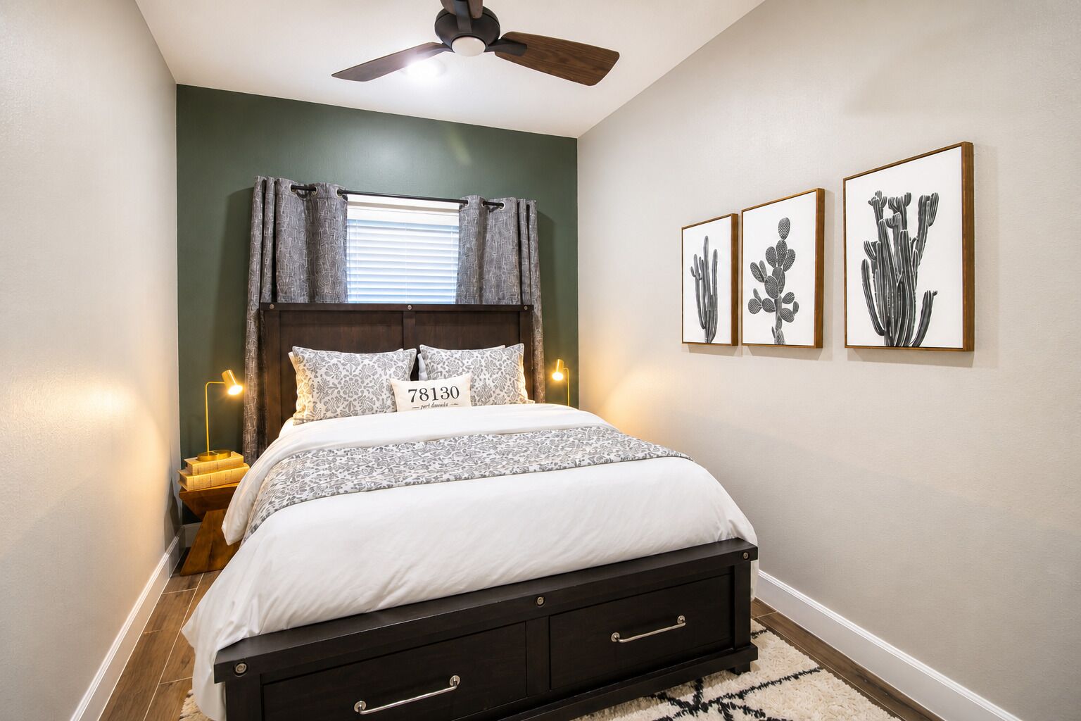 A bedroom with a bed, a ceiling fan, a nightstand with a lamp, and three framed pictures on the wall.