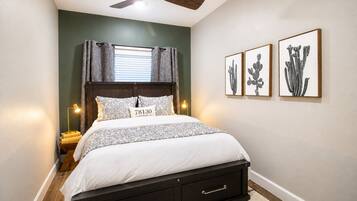 A bedroom with a bed, a ceiling fan, a nightstand with a lamp, and three framed pictures on the wall.