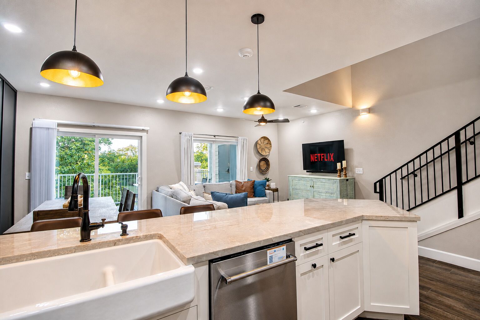 A modern kitchen with a dishwasher, a dining area with a table, and a living room with a sofa and a TV displaying 'NETFLIX'.