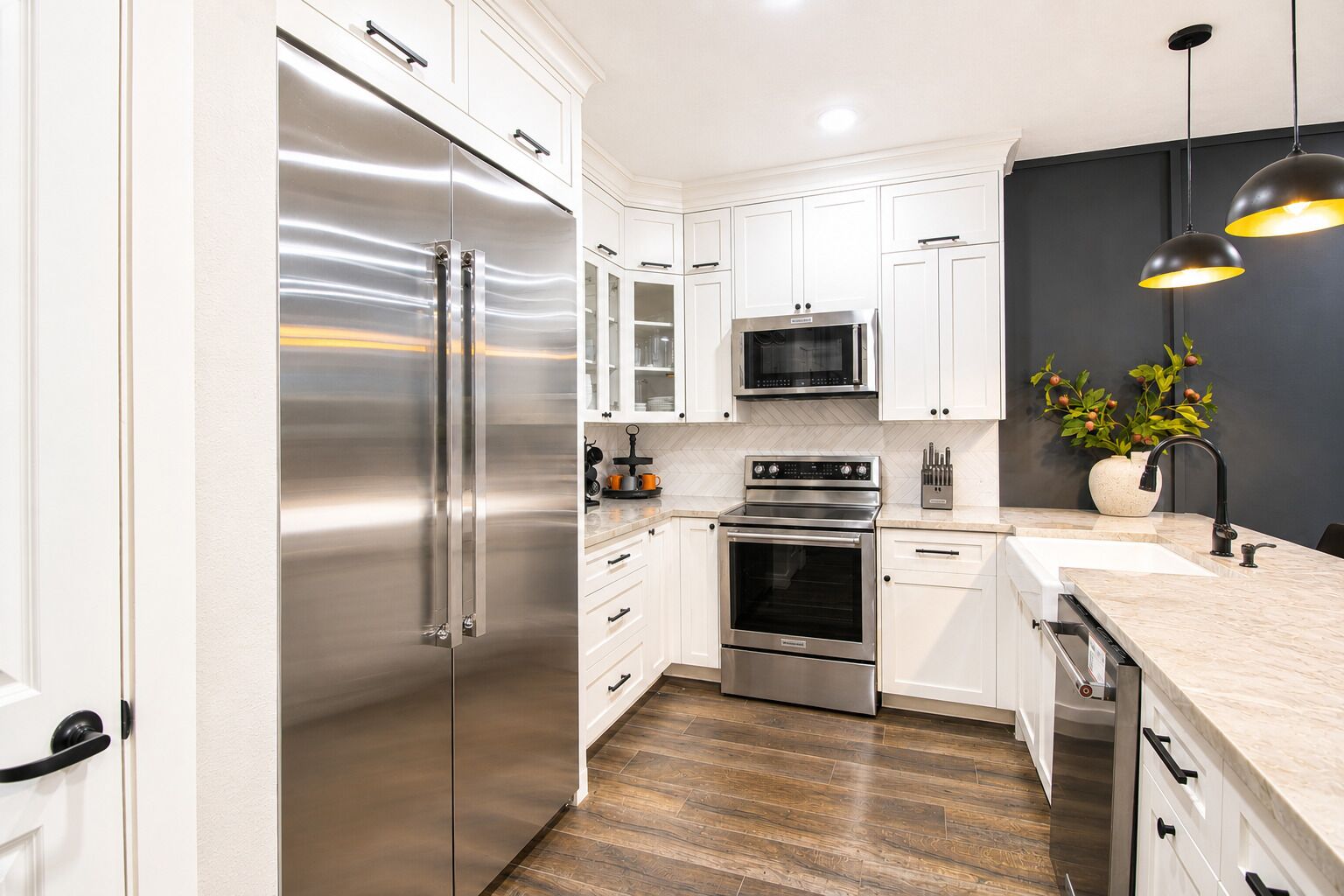 Une cuisine moderne dotée d’appareils électroménagers en acier inoxydable, de meubles blancs et d’un parquet en bois disposé en motif chevron.