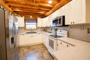Una cocina con armarios blancos, un refrigerador de acero inoxidable, un microondas y una estufa.