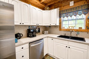 A kitchen with white cabinets, a stainless steel refrigerator, a coffee maker, a toaster, and a window with a decorative valance. - Charming dog-friendly home with expansive deck - near boat ramp & attractions (New Braunfels)