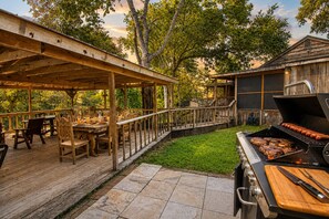 Une terrasse extérieure avec des tables et des chaises en bois, un barbecue et un espace de terrasse couvert.