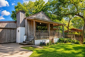 Une cabane en bois dotée d’un porche, entourée d’une végétation luxuriante et d’arbres.