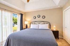 A bedroom with a bed, two bedside tables, a window with curtains, and a door. - 2BR Condo W/ Pool, Hot Tub, Grills, Walk to Schlitterbahn! (New Braunfels)