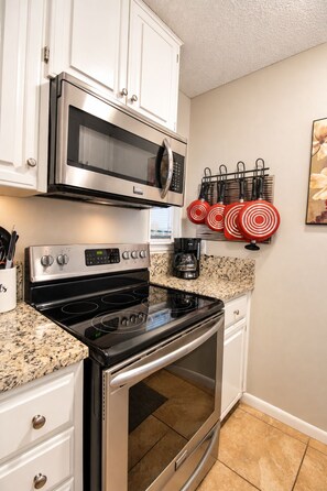 A kitchen with white cabinets, a stainless steel microwave, a black stove, and a coffee maker. - 2BR Condo W/ Pool, Hot Tub, Grills, Walk to Schlitterbahn! (New Braunfels)