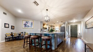 Una cocina amplia con una isla central, taburetes de bar y un comedor con sofá y sillas.