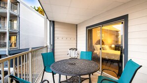 Ein Balkon mit rundem Tisch und Stühlen, eine Schiebetür zu einem Schlafzimmer und ein weißes Gebäude mit einem Balkon auf der linken Seite.