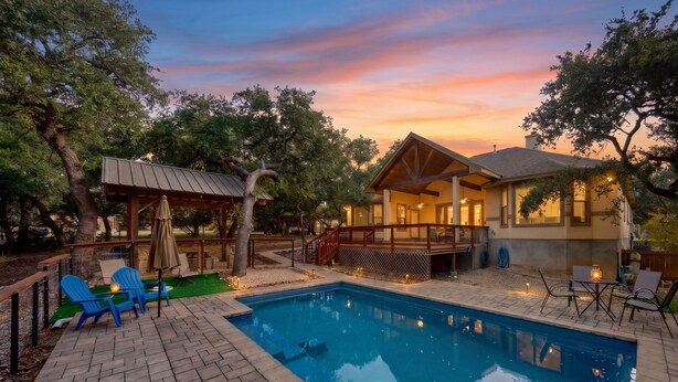 Zona de piscina con terraza de madera, sillas azules y un área de estar cubierta.