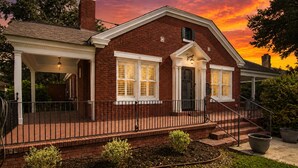 A brick house with a porch, a chimney, and a well-maintained garden.