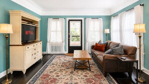 A living room with teal walls, a brown leather sofa, a wooden coffee table, a TV on a cabinet, and a patterned rug.