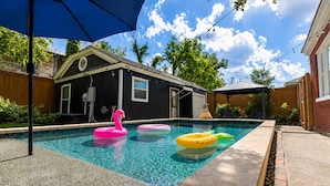 A swimming pool with three inflatable swans, a covered patio, and a house with a garage.