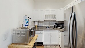 Una cocina compacta con armarios blancos, microondas, cafetera y refrigerador.
