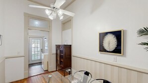 Un comedor con una mesa de vidrio, sillas, un ventilador de techo y una obra de arte enmarcada en la pared.