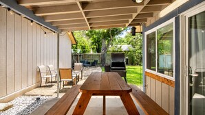 Un patio esterno con tavolo da picnic in legno, sedie e barbecue.