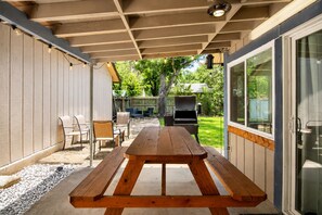 An outdoor patio with a wooden picnic table, chairs, and a grill. - Cozy Home | Pool Table & 2 Arcade Games | Enclosed Backyard (San Antonio)