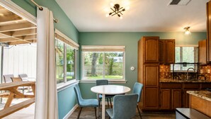 Una cucina con mobili in legno, un tavolo rotondo con sedie e vista sul giardino attraverso ampie finestre.