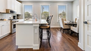 A modern kitchen with white cabinetry, a central island, and a dining area with chairs.