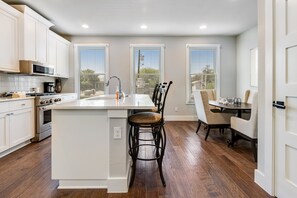 A modern kitchen with white cabinetry, a central island, and a dining area with chairs. - Downtown home with WiFi, central AC, furnished rooftop deck, and full kitchen (San Antonio)