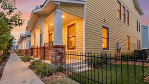 A residential building with a covered porch, brick steps, and a black metal fence.