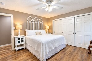 Une chambre à coucher comprenant un lit, des tables de chevet, un ventilateur de plafond et une armoire.