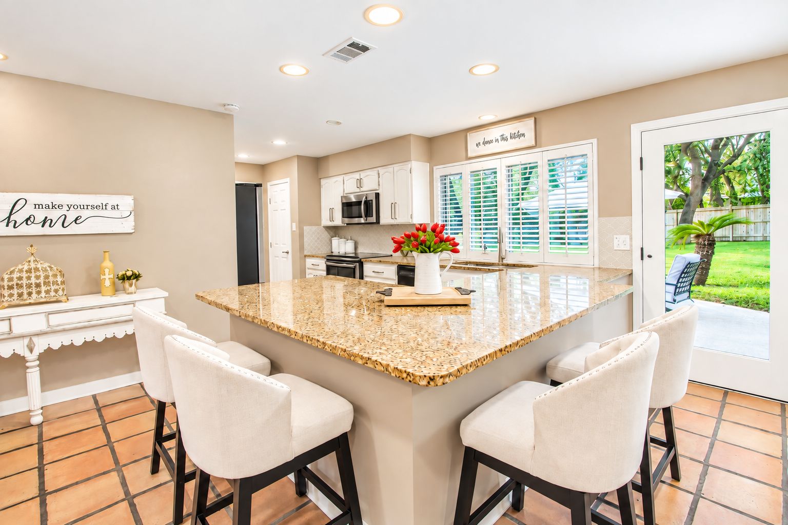 A modern kitchen with a central island, bar stools, and a view of the outdoors.