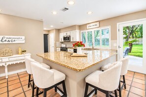 A modern kitchen with a central island, bar stools, and a view of the outdoors. - Dog-friendly chic home w/private outdoor pool, gas grill, & enclosed backyard (San Antonio)