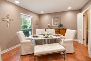 Une salle à manger avec une table ronde dressée pour quatre personnes, entourée de quatre chaises, d’un banc et d’un élément décoratif mural.
