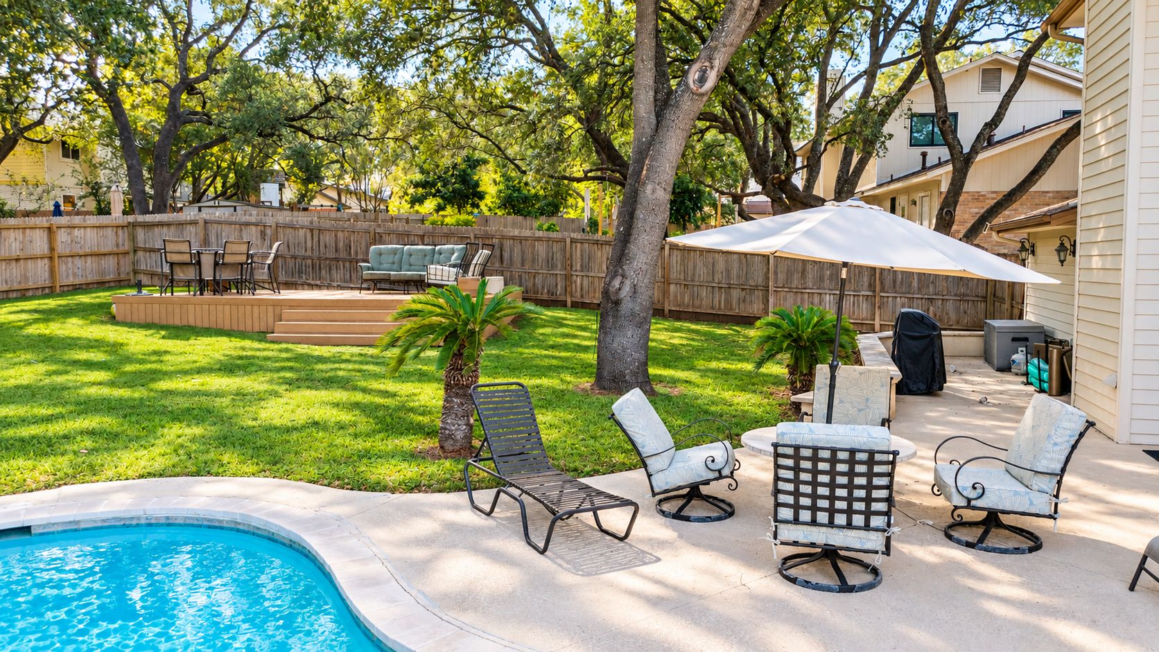 A backyard with a swimming pool, patio furniture, and a wooden fence.