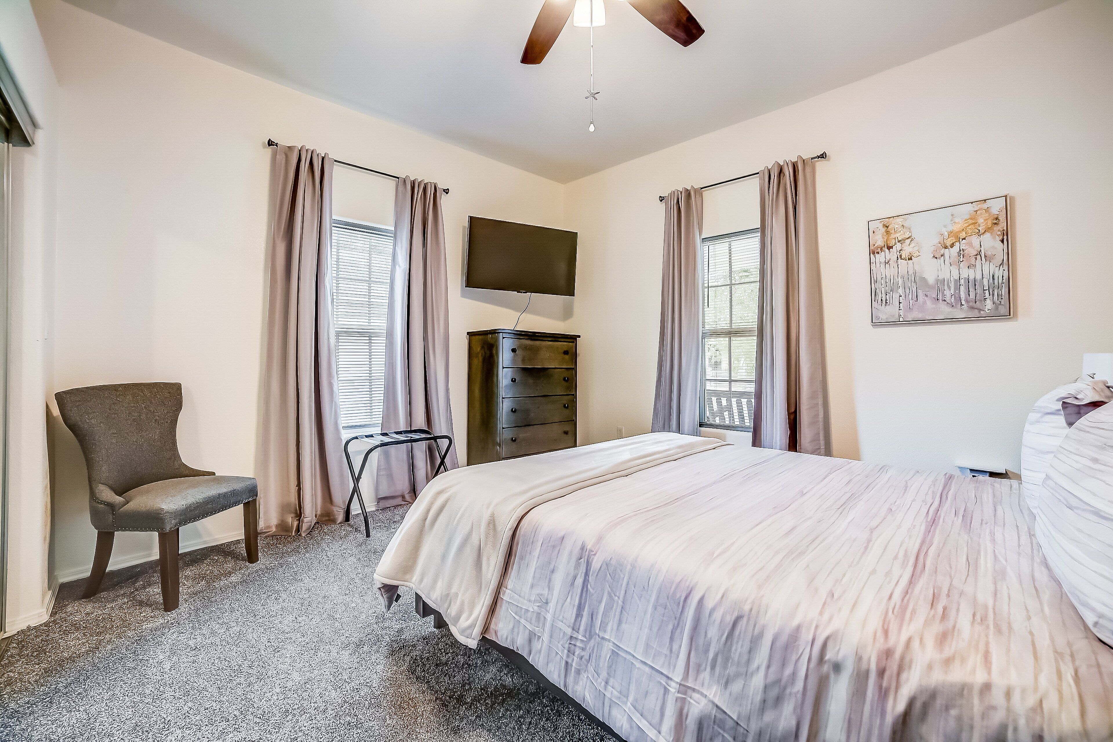 A hotel room with a bed, a chair, a TV, and a dresser.