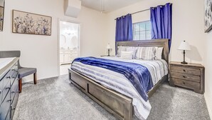 Een slaapkamer met een bed, een dressoir, een nachtkastje, een plafondventilator en een raam met gordijnen.